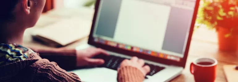 Person typing on a laptop beside a coffee cup.