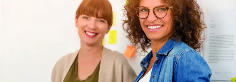Deux femmes souriantes dans un bureau avec des post-it sur le mur.