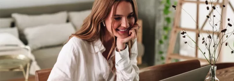 Femme souriante devant un ordinateur portable dans un salon moderne.