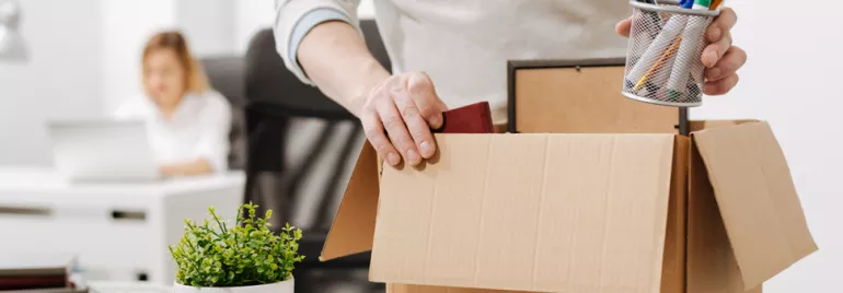 Person packing office supplies into a cardboard box.