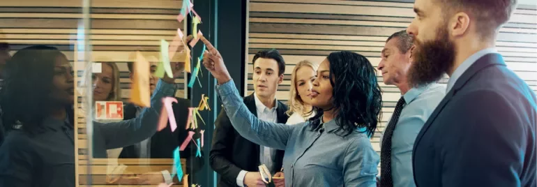 Team discussing in front of a glass wall with sticky notes.