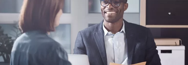 Two people having a meeting in an office setting, one holding a folder and smiling.