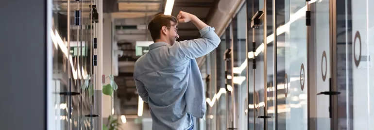 Man celebrating in modern office hallway.