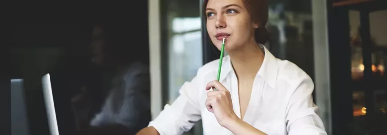 Femme pensant à un bureau avec un ordinateur portable, tenant un crayon.