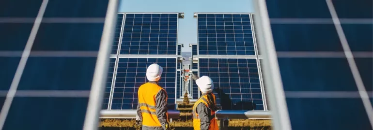 Two workers inspecting solar panels in a field on a sunny day.