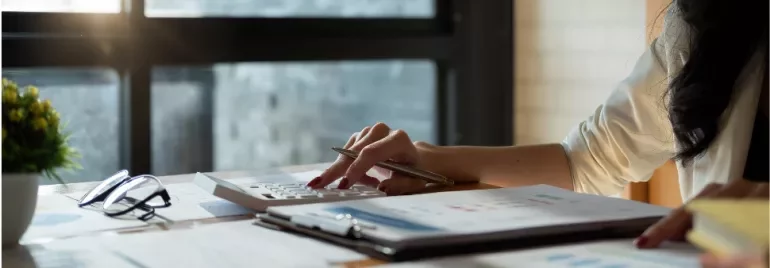 Person using calculator with papers and glasses on desk.