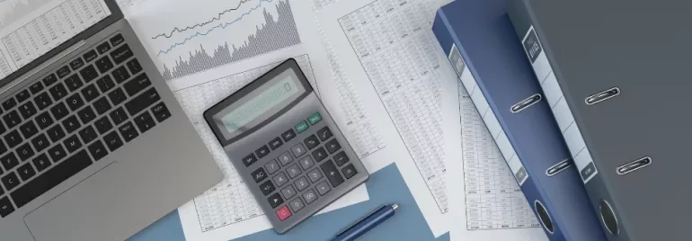 Laptop, calculator, and documents with charts and binders on a desk.