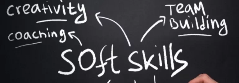 Hand writing 'soft skills' with words like creativity, coaching, and team building on a chalkboard.