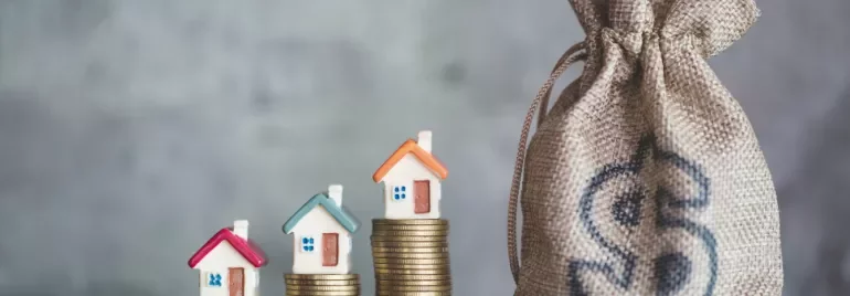Small houses on coin stacks beside a money bag.