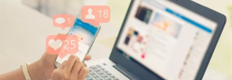 Person using a smartphone with social media notifications, next to a laptop.