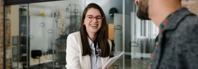 Woman in glasses smiles while shaking hands in a modern office.