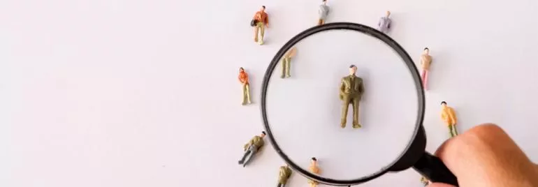 Magnifying glass focuses on miniature figure surrounded by others.