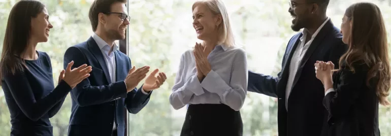 Group of colleagues applauding a smiling woman indoors.