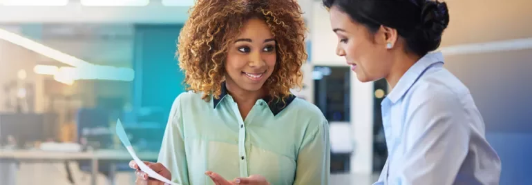 Two women talking and one holding a sheet of paper