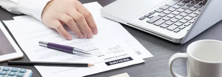 Person typing on laptop with documents, glasses, and a calculator on the desk.