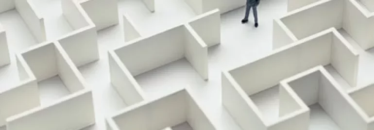A businessman stands in a large white maze, contemplating his path.
