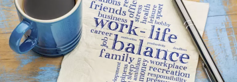 Coffee cup and pen next to napkin with 'work-life balance' word cloud.