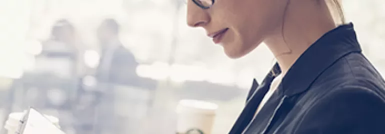 Femme avec des lunettes lisant une tablette dans un café.