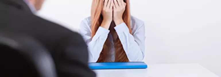 Personne à un bureau se couvrant le visage, semblant stressée.