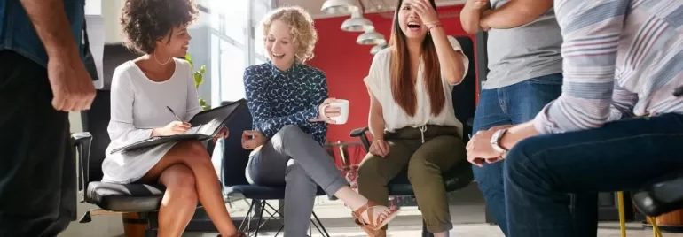 Group of colleagues laughing and talking in an office setting.