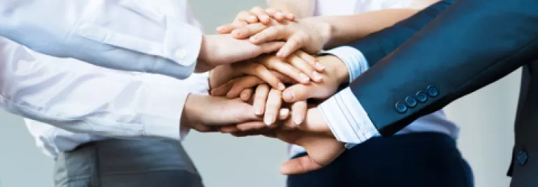 Group of people stacking hands together in teamwork.
