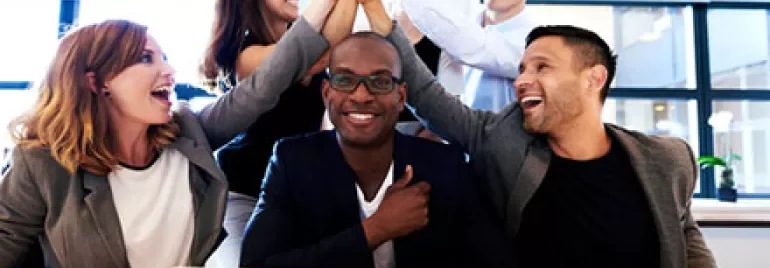 Group of colleagues celebrating a success with high-fives around a laptop.
