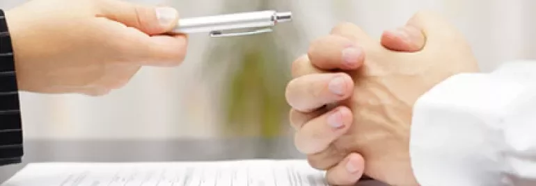 Deux mains au-dessus d'un document, l'une tendant un stylo, l'autre avec les doigts entrelacés.