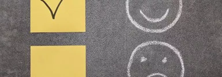 Yellow sticky notes with a checkmark, next to chalk-drawn happy and sad faces.