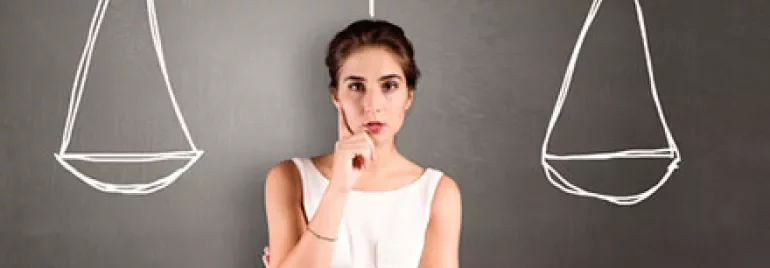 Woman contemplating in front of drawn balance scales on blackboard.