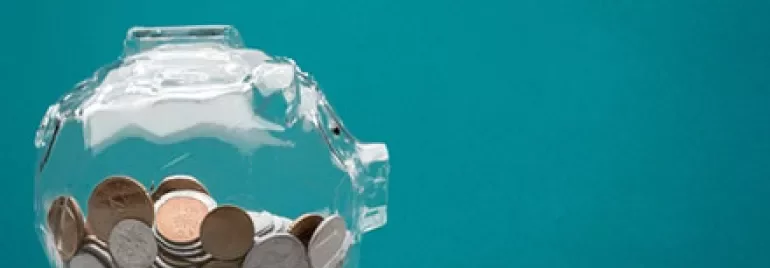 Transparent piggy bank filled with coins against a blue background.