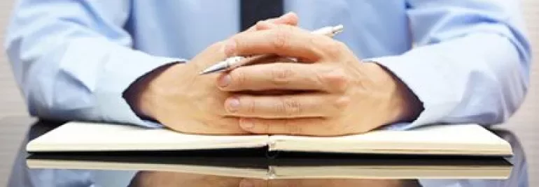Person in a blue shirt with hands clasped over an open notebook on a reflective table.