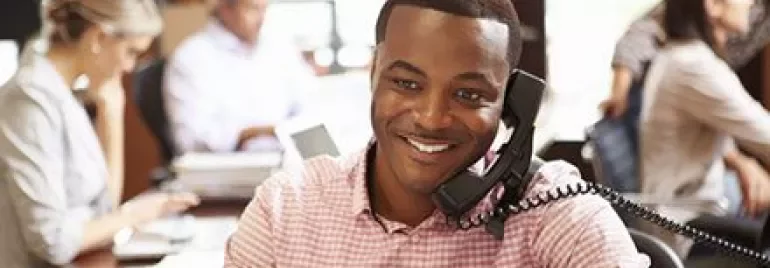 Man on phone smiling at desk in a busy office.