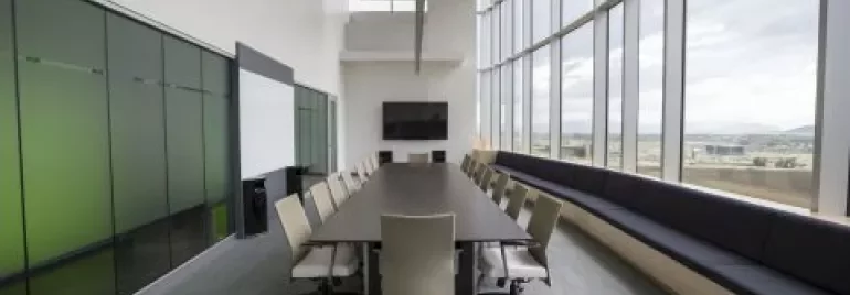 Salle de conférence moderne avec grande table et chaises près de fenêtres.