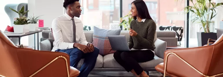 Two people talking on a sofa in a modern office.
