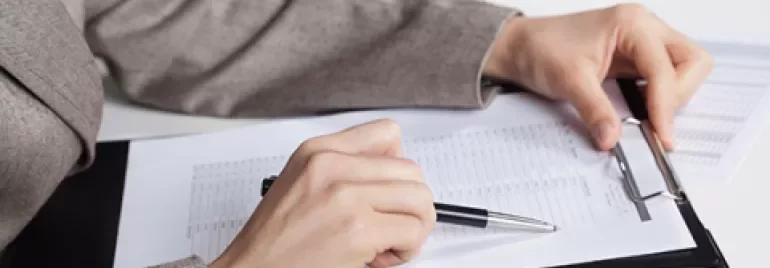 Person reviewing documents on a clipboard at a desk.