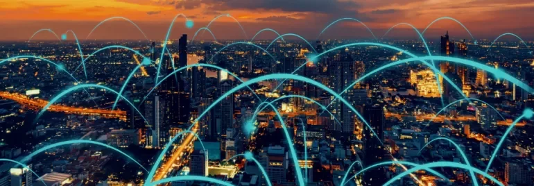 A city skyline at sunset with glowing digital network lines arching over buildings.