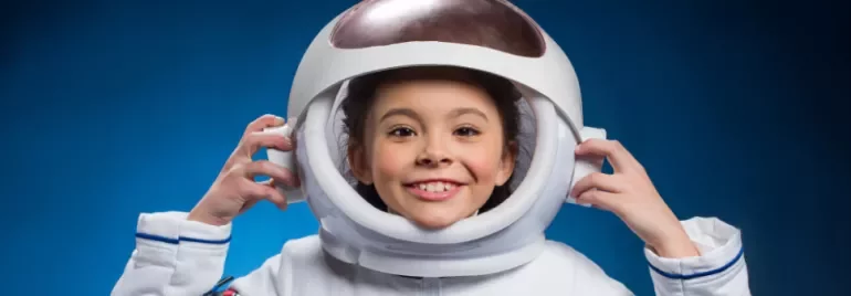 Child smiling in astronaut helmet against blue background.