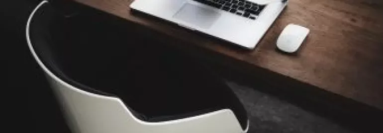 Laptop and mouse on wooden desk with modern chair.