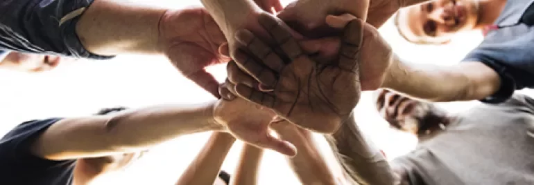 Group of people joining hands in a circle, symbolizing teamwork.