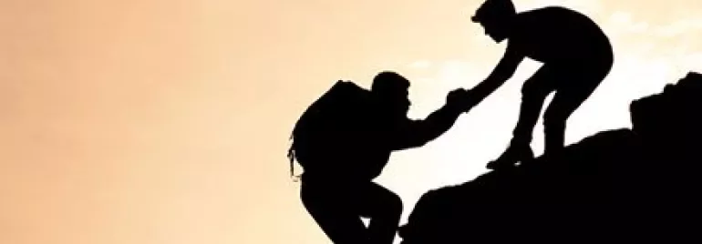 Two climbers silhouetted against a sunset, one helping the other up.