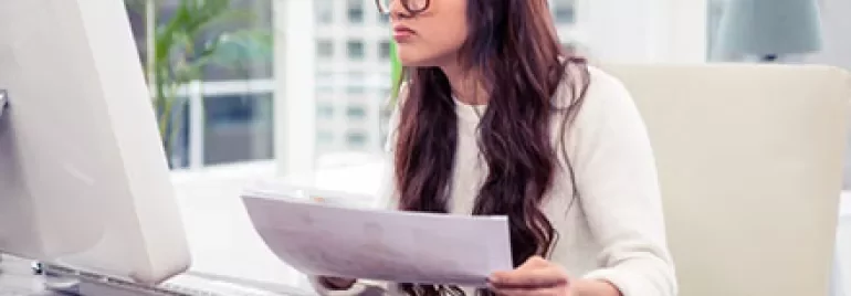 Woman at desk analyzing documents on computer.
