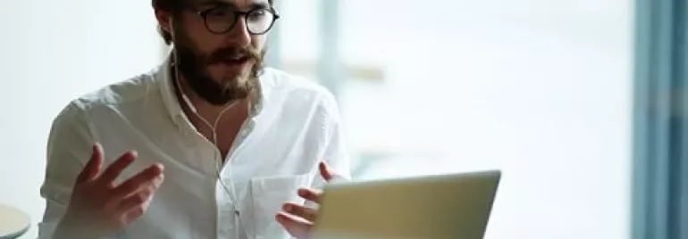 Man with glasses using laptop and headset in cafe.