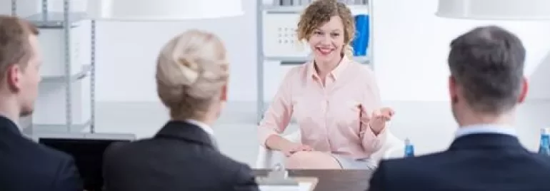 Woman speaking to interview panel in office setting.