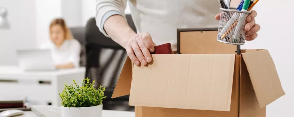 Person packing office supplies into a cardboard box.