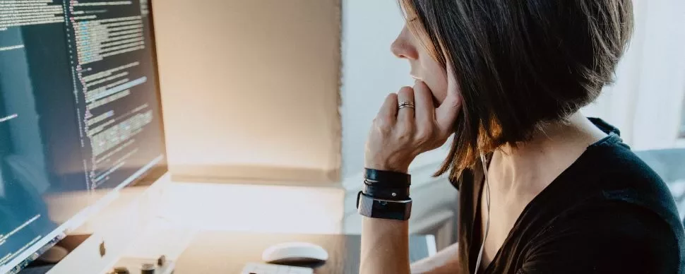 Femme concentrée sur un écran d'ordinateur affichant du code.