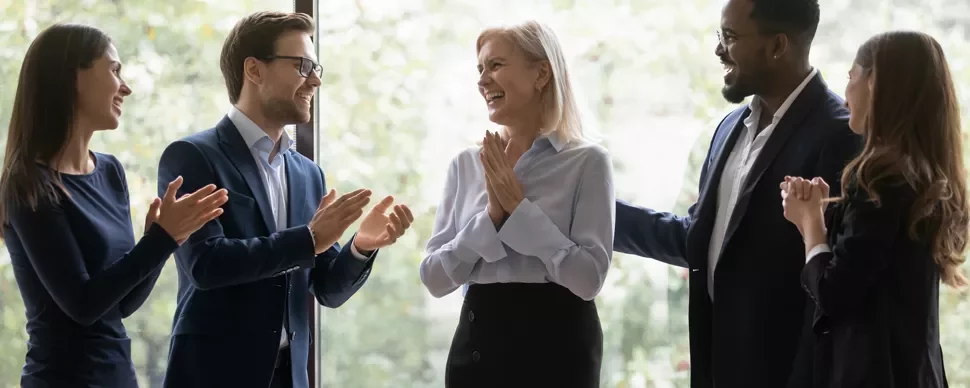 Groupe de collègues applaudissant une femme souriante à l'intérieur.