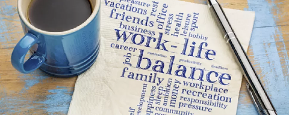 Coffee cup and pen next to napkin with 'work-life balance' word cloud.