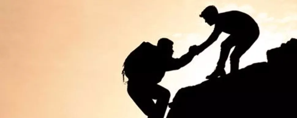 Two climbers silhouetted against a sunset, one helping the other up.