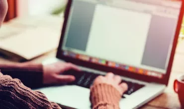 Person typing on a laptop beside a coffee cup.
