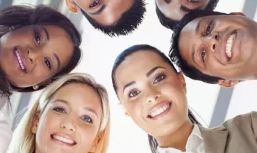 Group of six people smiling in a circle, looking down.